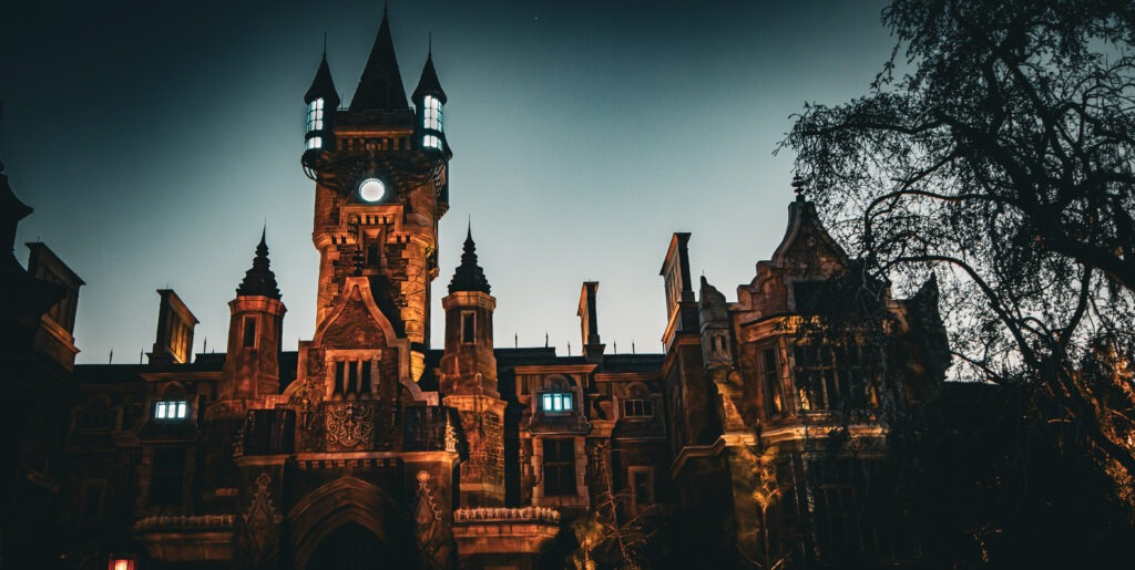 A gothic-style castle looms against the twilight sky, its tall spires and clock tower glowing with eerie illumination. The dramatic lighting casts deep shadows across the stone façade, enhancing its haunting and mysterious atmosphere.