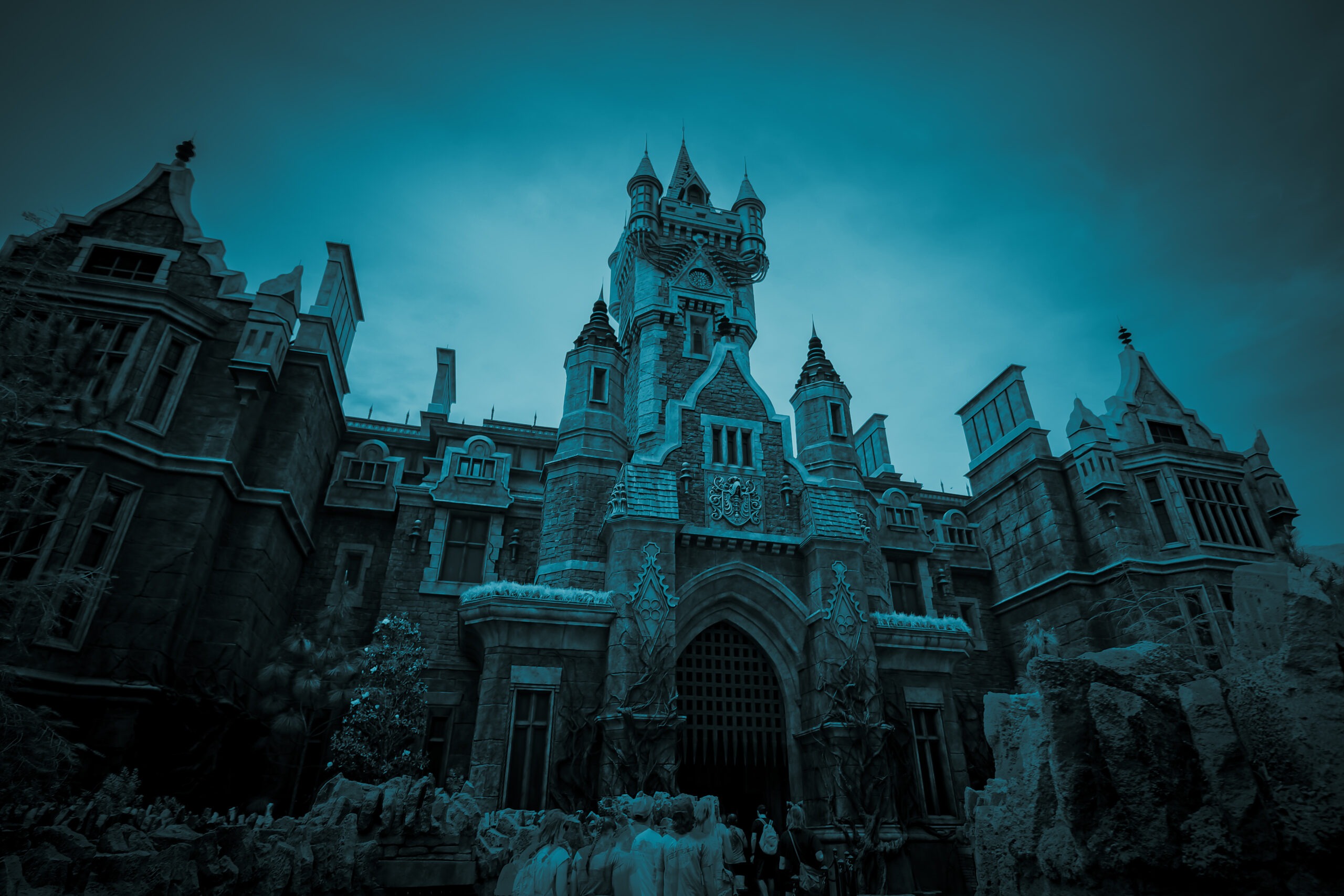 A towering Gothic-style castle with spires and arched windows looms under a moody, teal-tinted sky, giving it a haunted, otherworldly feel. At the base of the entrance, a group of ghostly, semi-transparent figures appear to be waiting or moving toward the dark, gated doorway, enhancing the eerie, supernatural atmosphere.