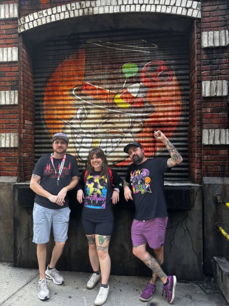 The Fear and Beer crew at their favorite event, Halloween Horror Nights. They stand in front of Major Sweet's haunted attraction which appeared at Halloween Horror Nights in 2024. 